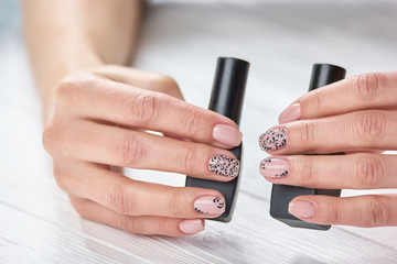 Perfect beige manicure with black lace. Caucasian womans hands with fresh manicure holding bottles...