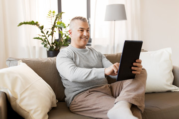 technology, people and lifestyle concept - man with tablet pc computer sitting on sofa at home