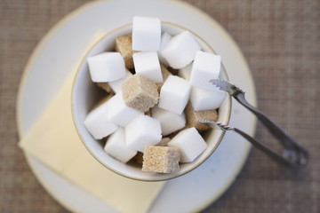 Close up white and brown sugar cubes in a bowl with a metallic pincers at the restaurant