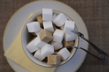 Close up white and brown sugar cubes in a bowl with a metallic pincers at the restaurant