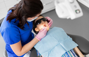 medicine, dentistry and healthcare concept - female dentist with mouth mirror checking for kid patient teeth at dental clinic