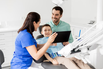medicine, dentistry and healthcare concept - dentist showing tablet pc computer to kid patient and his father at dental clinic