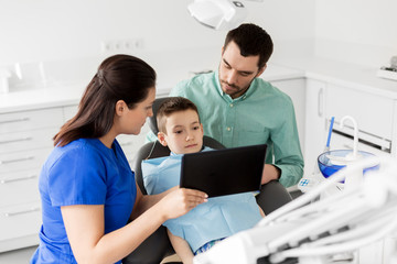 medicine, dentistry and healthcare concept - dentist showing tablet pc computer to kid patient and his father at dental clinic