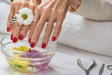 Female hands receiving spa procedure. Senior woman hands in aroma bath with colorful...