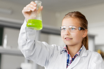 education, science and children concept - girl in goggles with test tube studying chemistry at school laboratory
