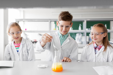 education, science, chemistry and children concept - kids or students with test tube making experiment at school laboratory