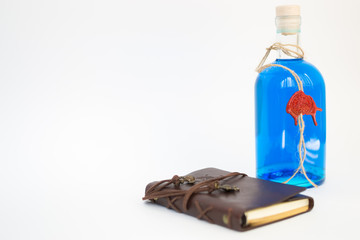 glass bottle with blue Curacao alcohol color on white background. brown leather notebook with white...