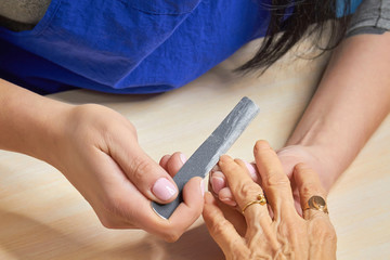 Manicurist filing nails to senior woman. Old woman hands in a nail salon receiving a manicure by a beautician with nail file. Elderly woman is getting a manicure in beauty salon.