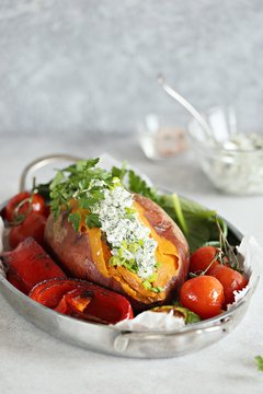 Oven baked sweet potato served with herbs cream cheese filling and roasted vegetables. Super food, clean eating, plant based concept.