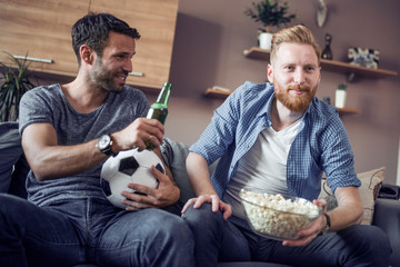 Two friends watch a football game at home