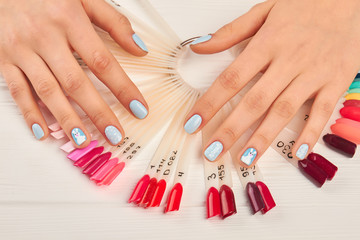 Obraz na płótnie Canvas Manicured hands and nails color palette. Gentle winter manicure and hand-pinted nail samples. Variants of nails design on artificial nail samples. Beautiful winter manicure.