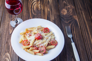 Italian penne pasta with tomatoes and wine on a wooden background