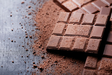Chocolate bars with cocoa powder on wooden table