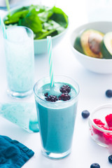 Blue Majik smooothie on tall glass with colored straw, over a blue colored wooden board against a clear background