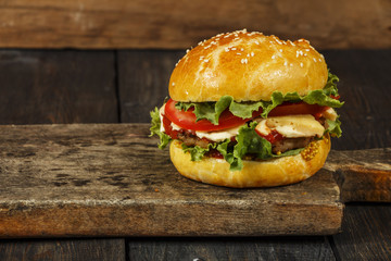 Hamburger on a wooden board against a dark background with copy space. Hamburger with sauce and fresh vegetables on a wooden table. Burger.