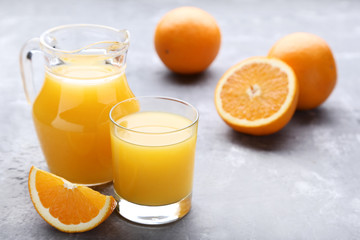 Fototapeta na wymiar Orange fruit with jug and glass of juice on grey wooden table