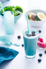 Blue Majik smooothie on tall glass with colored straw, over a blue colored wooden board against a...