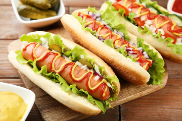Hot dogs with ketchup, mustard and vegetables on wooden table