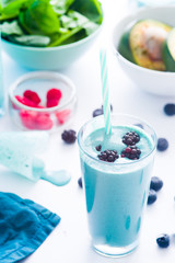 Blue Majik smooothie on tall glass with colored straw, over a blue colored wooden board against a clear background
