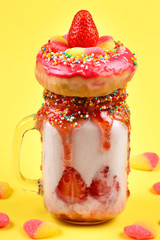 Freakshake. Extreme milkshake with strawberry, jelly sweets, donut on lilac background.