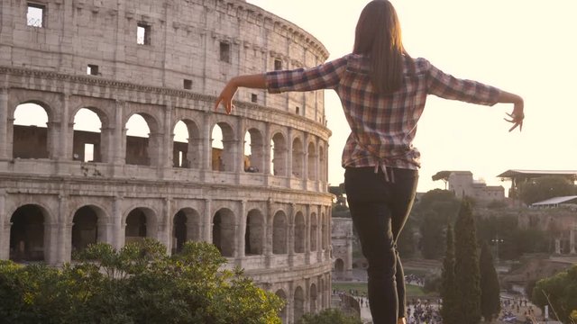 Romantic young couple tourists doing famous TITANIC scene in front of colosseum in rome at sunset boyfriend holding girlfriend spread arms happy beautiful woman long hair slow motion sun flair