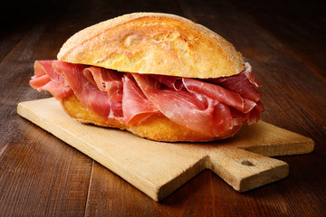 Sandwich with raw ham and cutting board on wooden background, closeup.