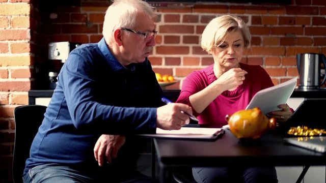 Senior worried couple counting bills sitting in the kitchen
