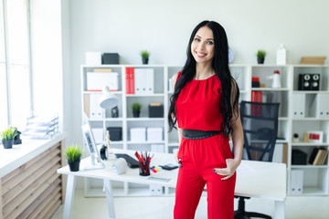 Beautiful young girl in a red suit is standing in the office.