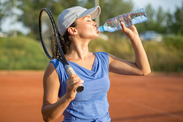 Beautiful young tennis player drinking water