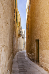 Fototapeta na wymiar Narrow limestone street with a lantern in the distance in Mdina, Malta