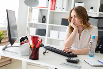 Beautiful young girl sits in the office and looks at the monitor.