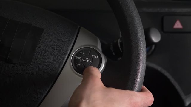 Finger pressing on buttons placed on the steering wheel of a car to control different settings like the volume, climate control, cruise control etc.