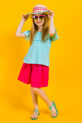 Girl with red hair on a yellow background. A charming girl in bright summer clothes holds her hand for her hat.