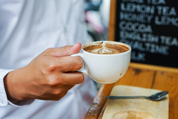 Man hand holding a Latte Art coffee mug.