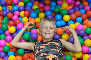Fototapeta na wymiar The boy lies, buried in the colorful balls of the game room.