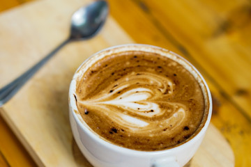 Latte art coffee heart picture placed on wooden tray, on the wooden table background.