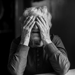 An elderly woman covers her face with wrinkled hands. Black and white photo.