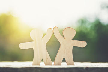 Wooden little men holding hands on natural sunlight background. Symbol of friendship, love and teamwork