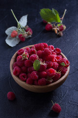 Raspberries in wooden bowl on black background. Fresh ripe sweet berries, healthy food
