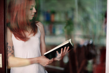 young woman reading a book at home in front of a window, natural moody shot