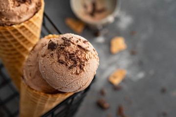 Homemade chocolate ice cream in waffle cones, with a spoon for ice cream, cocoa and pieces of dark chocolate. On a dark gray table. Copy space close view
