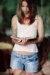 young woman reading a book at home in front of a window, natural moody shot