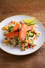 Roasted salmon fish with tomato couscous, zucchini and lime on white plate. vertical