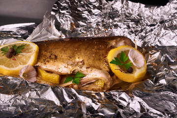 Baked fish with lemon, spices and herbs in baking sheet on wooden background without head