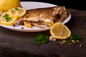 delicious roasted carp fish with lemon slices, spices, and fresh rosemary on white plate, view from above, close-up