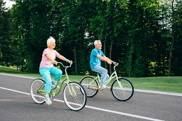 Senior couple riding bicycles on green park
