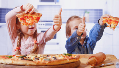 Two little female friends holding pizza slices as symbol of best food. Happy children having fun eating dinner.