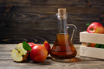 Apple cider vinegar and fresh red apple on a wooden background