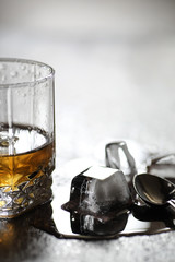 Whiskey in a glass and pieces of ice on a wood