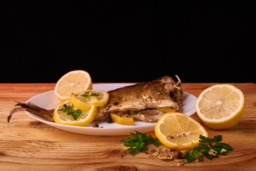 delicious roasted carp fish with lemon slices, spices, and fresh rosemary on white plate, view from above, close-up